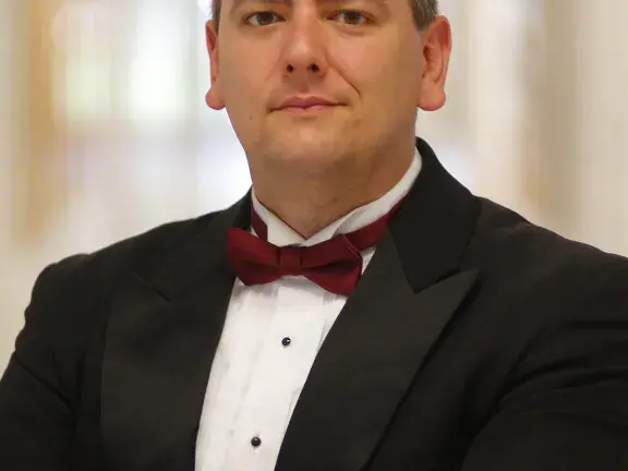 A photo of Dr. Vernon Huff. He is wearing a black suit with a red bow tie. His arms are crossed and he is looking at the camera.